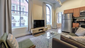 A modern apartment with a living room, TV, glass coffee table, sofa, and kitchen area with a fridge and microwave. - Bold, Spacious 2br in Boston`s Financial District (Boston)
