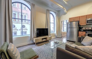 A modern apartment with a living room, TV, glass coffee table, sofa, and kitchen area with a fridge and microwave. - Bold, Spacious 2br in Boston`s Financial District (Boston)