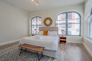 A bedroom with a large bed, two bedside tables, a bench, and two windows with blinds. - Milk153-3B-2/2 · Cozy 2br in Boston FIDI District (Boston)