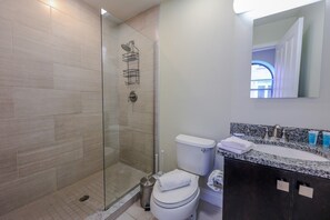 A bathroom with a glass shower enclosure, a toilet, a sink with a granite countertop, and a mirror above the sink. - Milk153-3B-2/2 · Cozy 2br in Boston FIDI District (Boston)