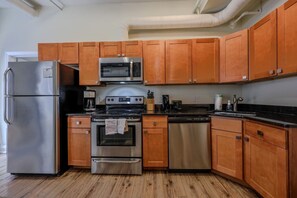 A kitchen with wooden cabinets, stainless steel appliances, and a black countertop. - Milk153-3B-2/2 · Cozy 2br in Boston FIDI District (Boston)