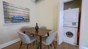 Un comedor con una mesa, sillas, un jarrón, un cuadro y una lavadora.