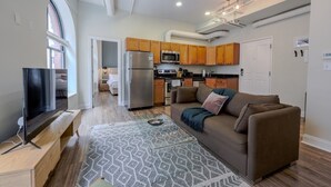 Un espacio habitable compacto con kitchenette, un sofá, un televisor y una alfombra estampada.