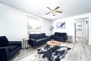 A modern living room with a dark blue sofa, a round coffee table, and a ceiling fan. - 245 Elliott · Centrally located 3BDRM home in CityCore! (Windsor)