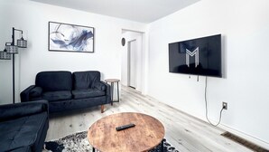 En moderne stue med en sort sofa, et træ sofabord, et ophængt fjernsyn og abstrakt kunst på væggen.