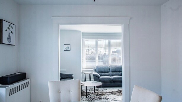 A modern living room with a glass table, two chairs, a grey sofa, and a large window with blinds. - 1036 Assumption · Bright 3 BDRM Unit Perfect for Longer Stays (Windsor)