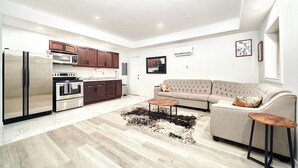 Ett modernt kök med rostfria vitvaror, en matplats med ett träbord och ett vardagsrum med en beige soffa.