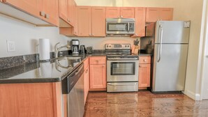 A kitchen with wooden cabinets, stainless steel appliances, a countertop with a coffee maker, and a refrigerator. - Milk153-3D-2/2 · 2br/2ba FIDI Apt | Keyless Entry | Walk anywhere! (Boston)