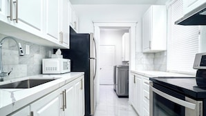 A modern kitchen with white cabinets, stainless steel appliances, and a marble backsplash.