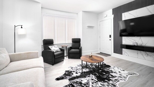 A modern living room with a sofa, two armchairs, a coffee table, and a TV mounted on the wall.