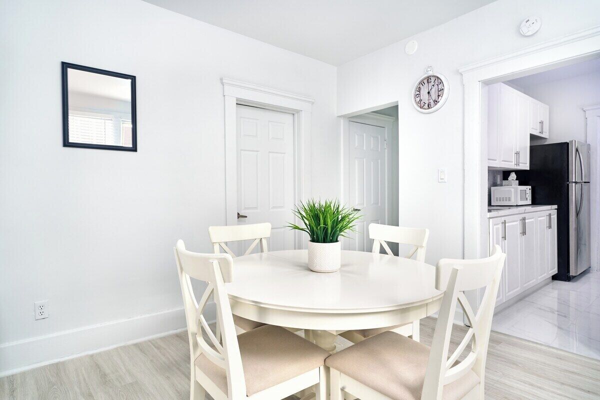 Un coin repas avec une table ronde, quatre chaises, une plante en pot et une horloge au mur.