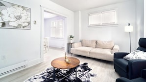 A modern living room with a sofa, a coffee table, and a lamp. There is a door leading to another room.