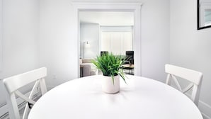 A white dining table with a potted plant, white chairs, and a white wall.