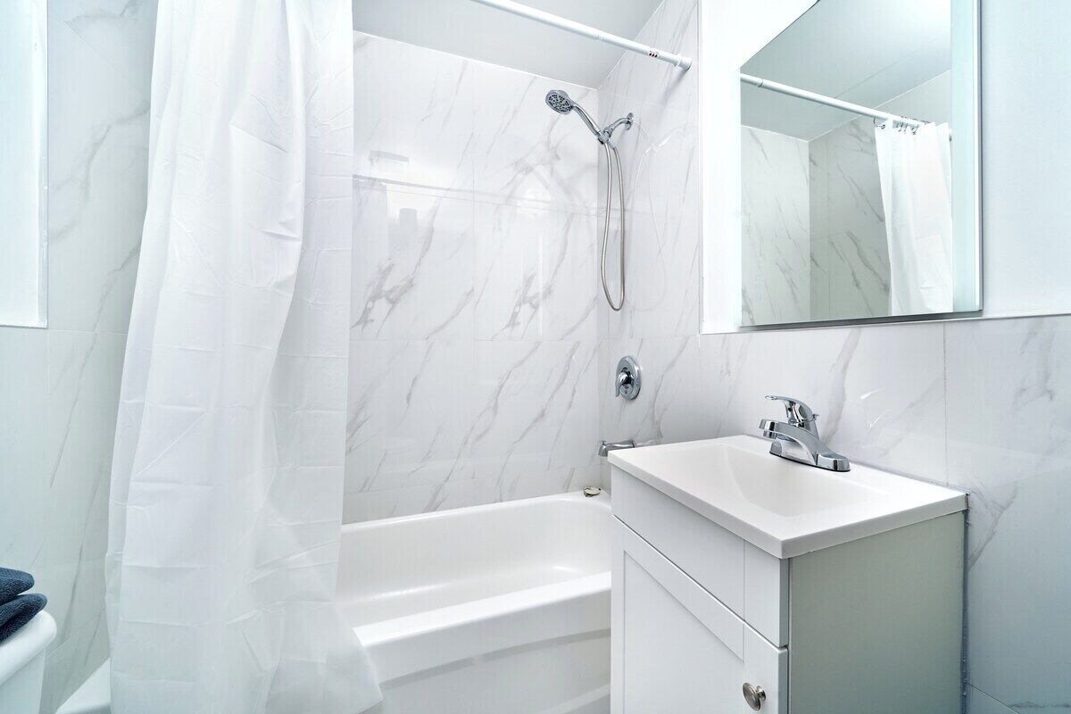 A modern bathroom with a white bathtub, a shower with a handheld showerhead, a vanity with a sink, and a large mirror.