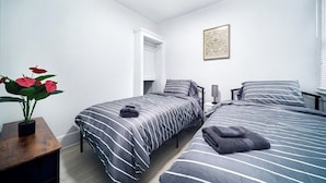 A bedroom with two beds, a bedside table, a potted plant, and a framed picture on the wall.