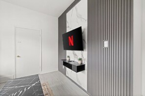 A modern hallway with a marble wall, a mounted TV displaying the Netflix logo, and a black shelf with two potted plants. - 804 · New Build Bright 2 Bdrm Unit (Windsor)