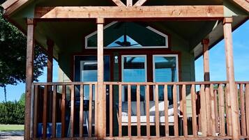 A wooden cabin with a balcony, a covered porch, and a small outdoor seating area.