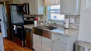 Cozinha moderna com eletrodomésticos de aço inoxidável, bancada de granito e vista para o exterior pela janela.