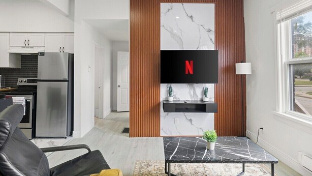 A modern kitchen with stainless steel appliances, a marble backsplash, and a flat-screen TV mounted on a wooden panel. - 219 · New Build Cozy 2 Bedroom Unit (Windsor)