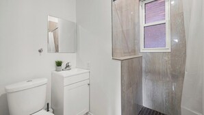A bathroom with a toilet, sink, mirror, and shower area. - 219 · New Build Cozy 2 Bedroom Unit (Windsor)