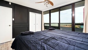 A bedroom with a large bed, a ceiling fan, and a view of the beach through large windows. - 902 - Stylish Waterfront Executive Condo (Windsor)