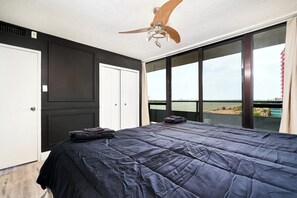 A bedroom with a large bed, a ceiling fan, and a view of the beach through large windows. - 902 - Stylish Waterfront Executive Condo (Windsor)