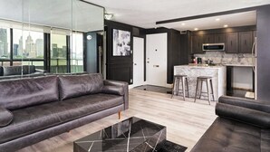 A modern living room with a dark leather sofa, a black marble coffee table, and a city view through large windows. - 902 - Stylish Waterfront Executive Condo (Windsor)