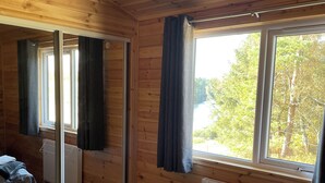 Habitación tipo cabaña de madera con cama, radiador y ventana con cortinas.