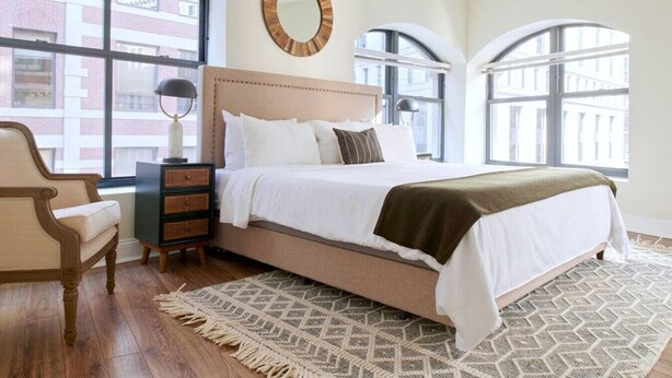 Una camera da letto con un letto grande, una cassettiera, una sedia e una finestra che si affaccia su edifici.
