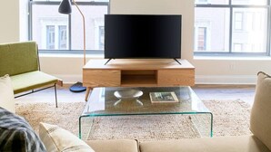 Un soggiorno moderno con una TV a schermo piatto su un mobile in legno, un tavolino in vetro e una poltrona verde.