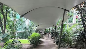 A concrete pathway under a white canopy, surrounded by lush greenery and rocks.