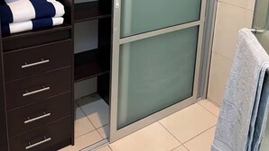 A bathroom with a dark wooden vanity, a glass shower enclosure, and a towel on the floor.