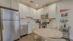 Una cucina con mobili bianchi, elettrodomestici in acciaio inossidabile, un tavolo da pranzo con sedie e uno stendardo del Boston College appeso al muro.