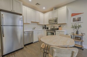 A kitchen with white cabinets, stainless steel appliances, a dining table with chairs, and a Boston College banner on the wall. - Warm 1BR in Boston FIDI | Close to Everything! (Boston)