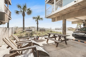 A beachside patio with wooden chairs and picnic tables, a palm tree, and a car parked nearby. - Heated Pool, Hot Tub & Steps to Beach | Ocean View (Gulf Shores)