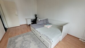 Quarto com cama, mesa de cabeceira, cadeira e radiador.