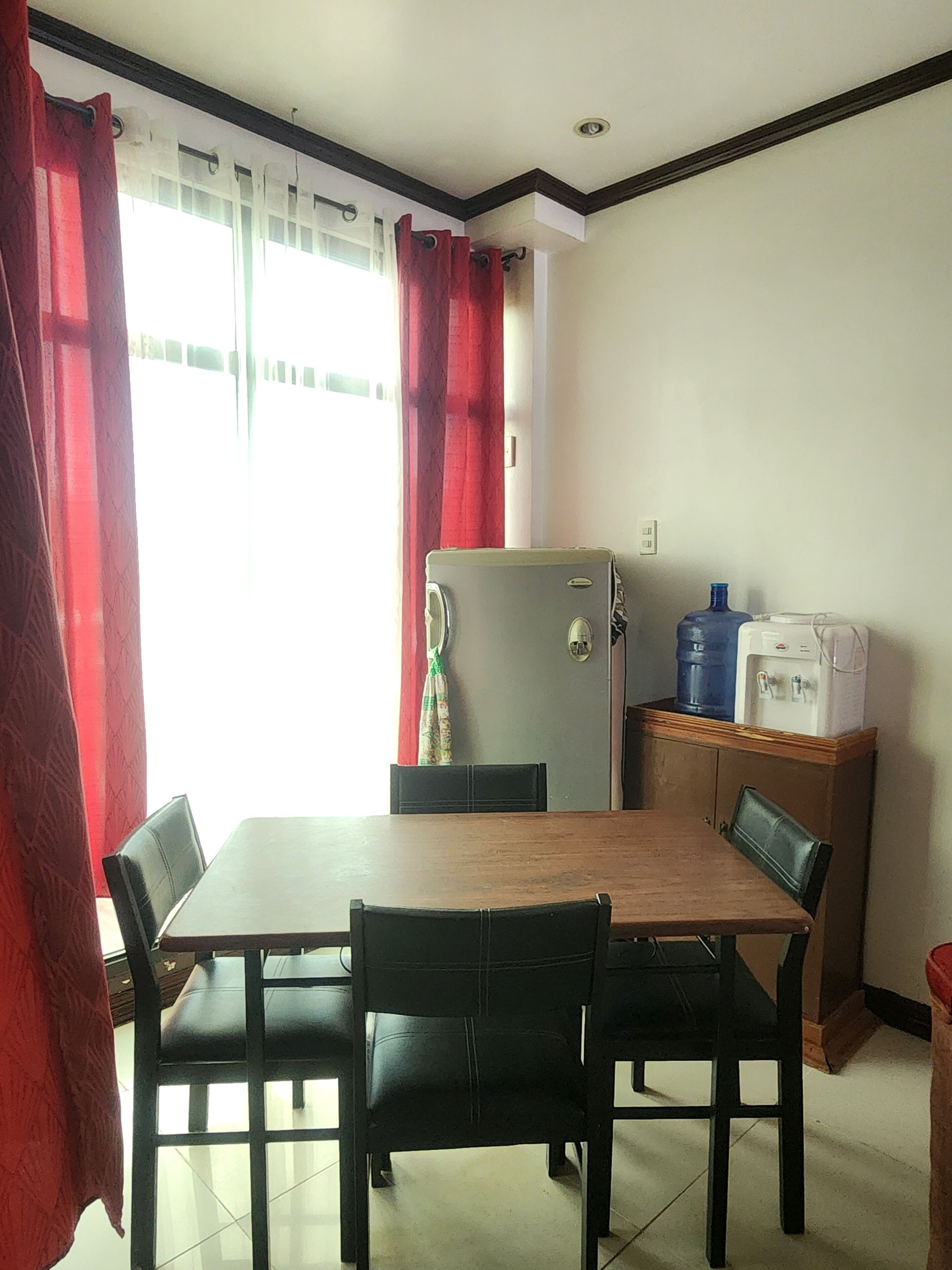 A dining area with a table and chairs, a refrigerator, and a water dispenser.