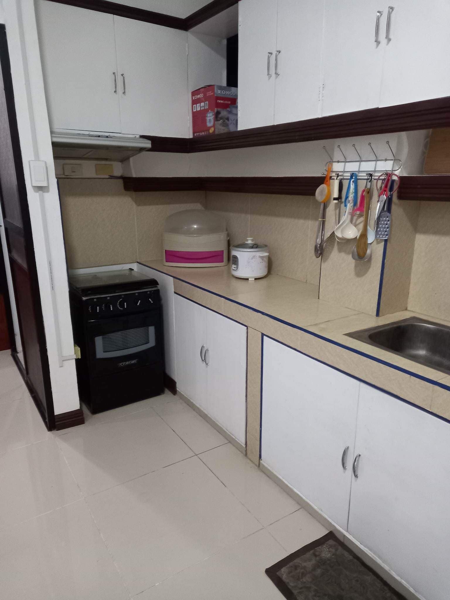 A compact kitchen with white cabinets, a stove, a rice cooker, and a sink.
