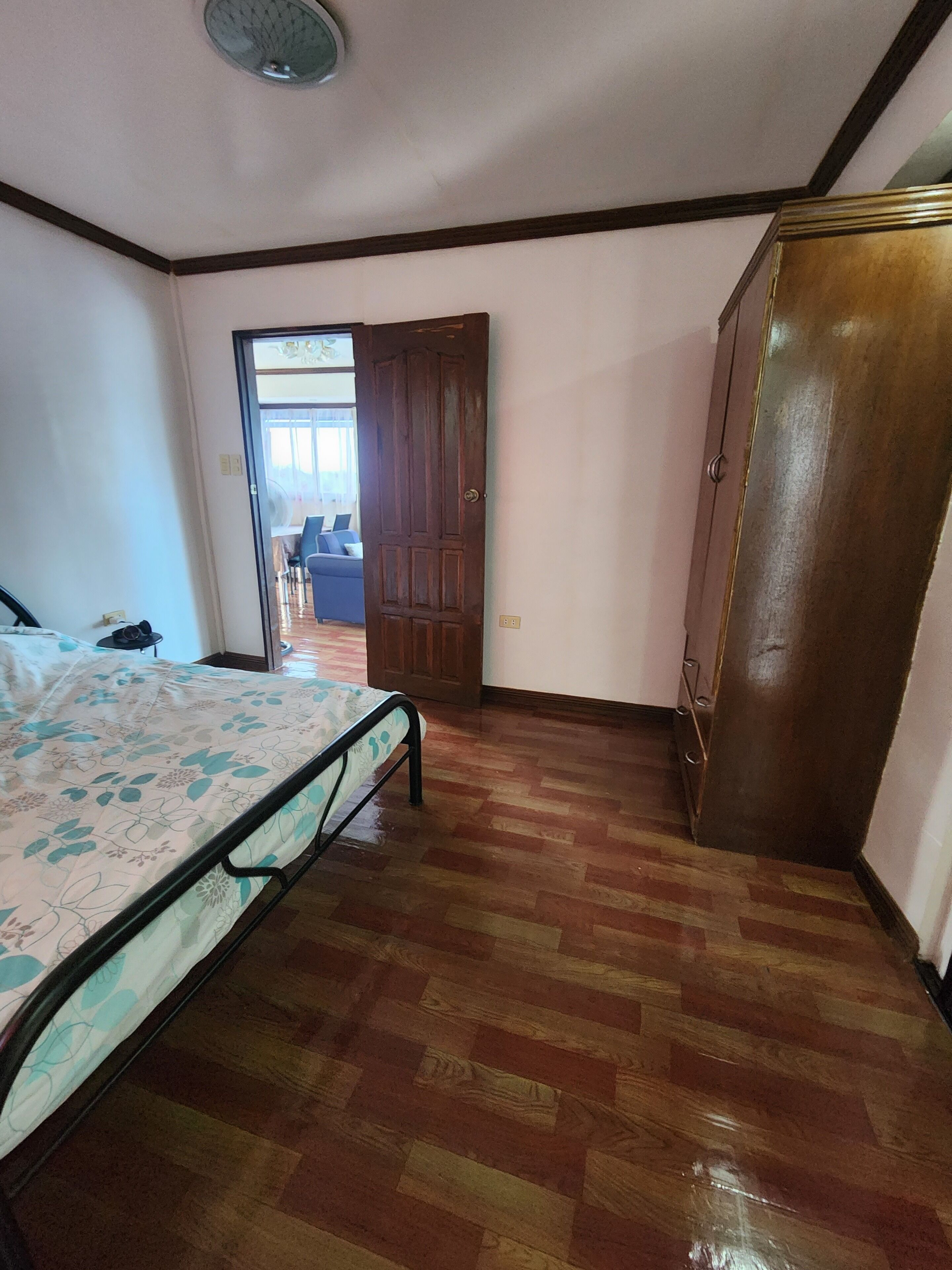 Een slaapkamer met een bed, een houten garderobe en een deur naar een andere kamer.