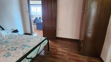 Een slaapkamer met een bed, een houten garderobe en een deur naar een andere kamer.