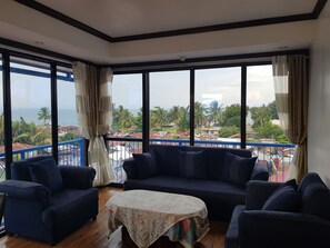 A spacious living room with a large window offering a view of the sea and palm trees.