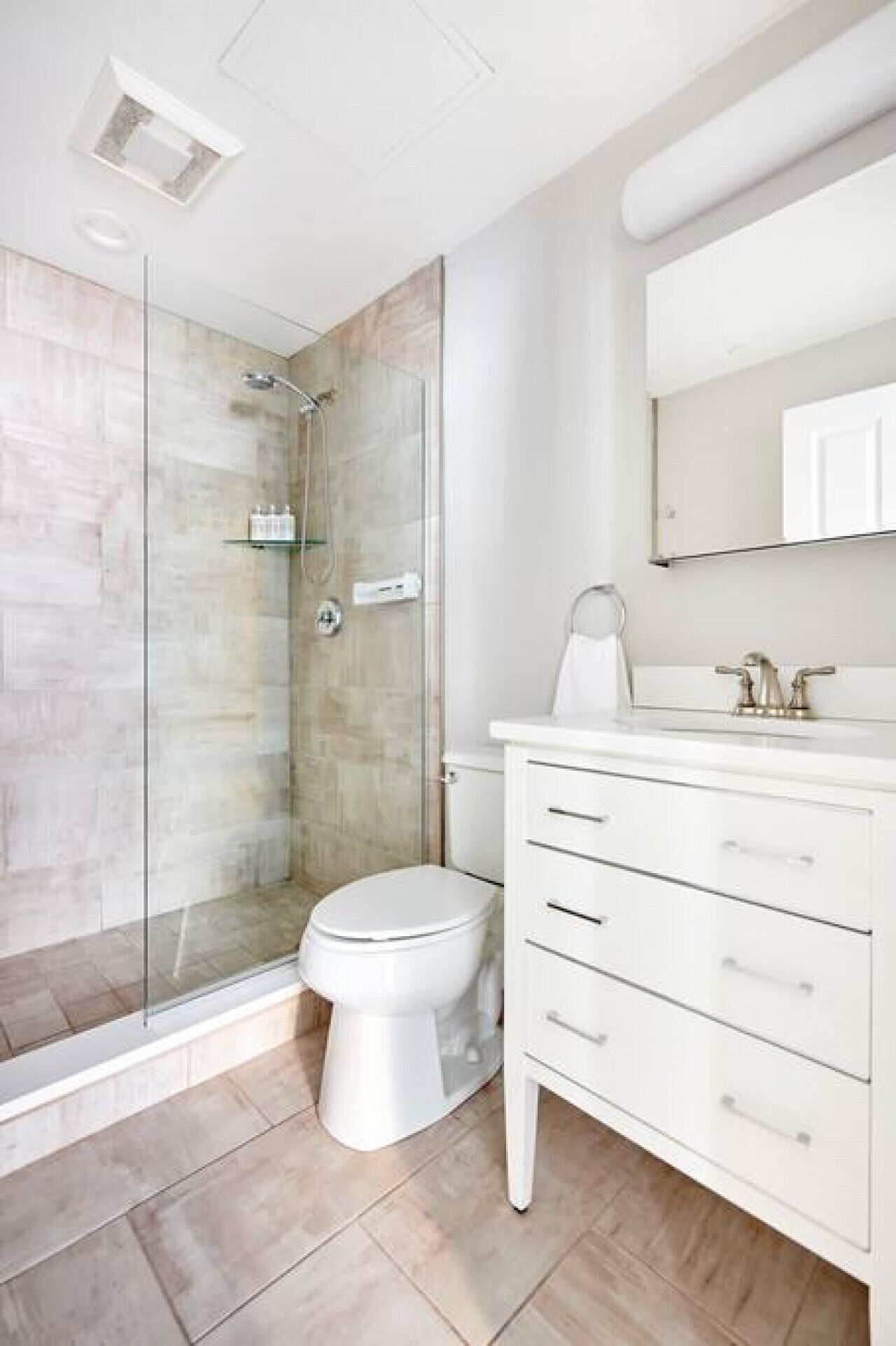 A modern bathroom with a glass-enclosed shower, a toilet, and a white vanity with drawers.