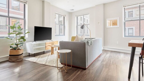 Un salon moderne avec un canapé gris, un téléviseur à écran plat, une petite table ronde et une plante en pot.