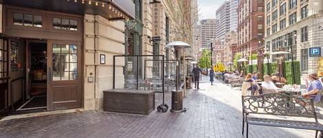 A street with outdoor seating, a building with a 'PUBLIC HOUSE' sign, and a 'BOSTONIA' sign on a pole.