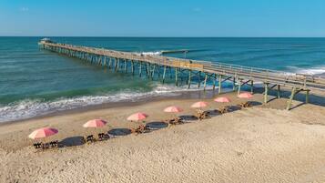 A beach with a wooden pier extending into the ocean, accompanied by beach chairs and umbrellas.