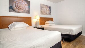 A hotel room with two beds, white bedding, wooden headboards, and two large spiral shell paintings on the wall. - Oceanana Motel (Atlantic Beach)