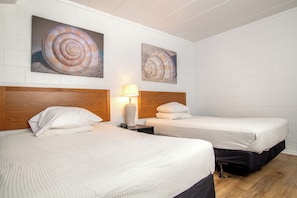 A hotel room with two beds, white bedding, wooden headboards, and two large spiral shell paintings on the wall. - Oceanana Motel (Atlantic Beach)