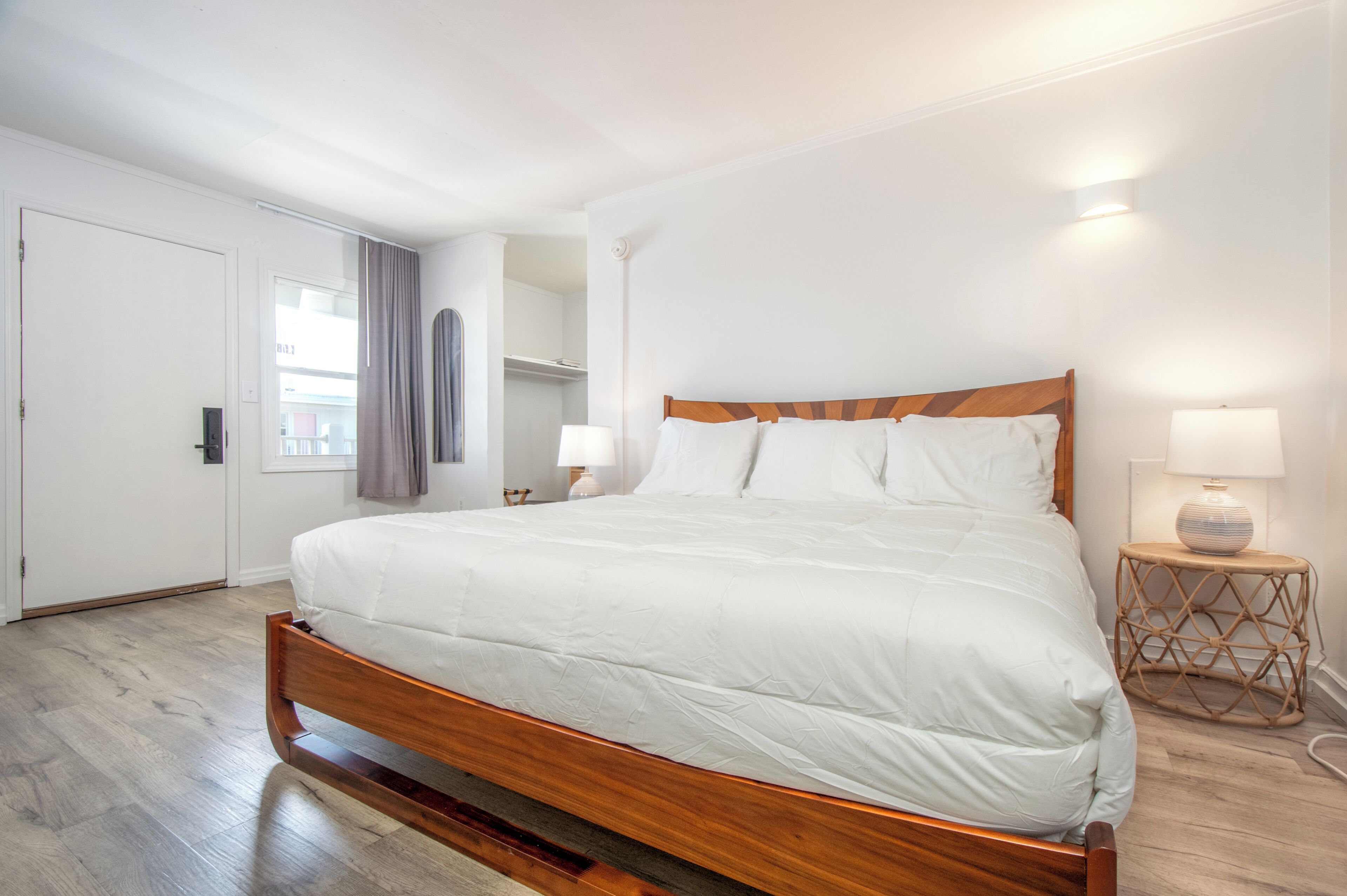 A bedroom with a wooden bed, a bedside table with a lamp, a wardrobe, and a window with curtains.