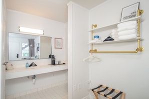 A bathroom with a white sink, a mirror, a towel rack with towels, and a hanging garment. - Oceanana Motel (Atlantic Beach)