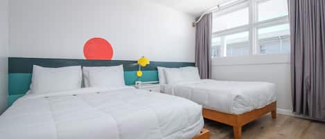 A hotel room with two beds, a window with curtains, a wall with a red circle and a yellow star, and a wooden floor.
